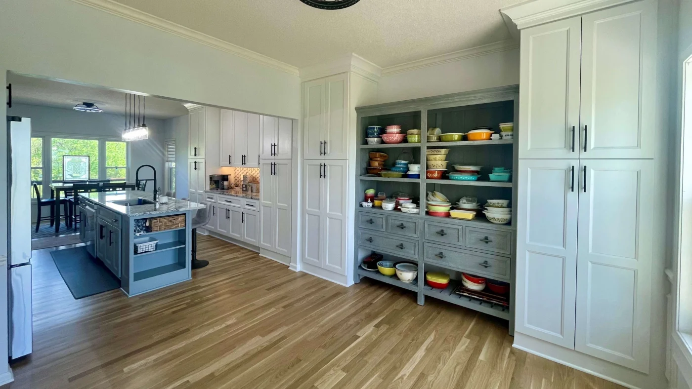 A spacious kitchen remodel with a large gray kitchen island, light countertop, tall white cabinets, and hardwood flooring.