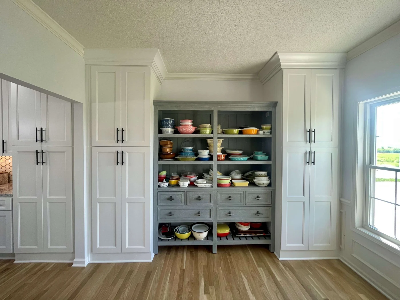An open space in a kitchen containing gray cabinets with four shelves holding bowls.