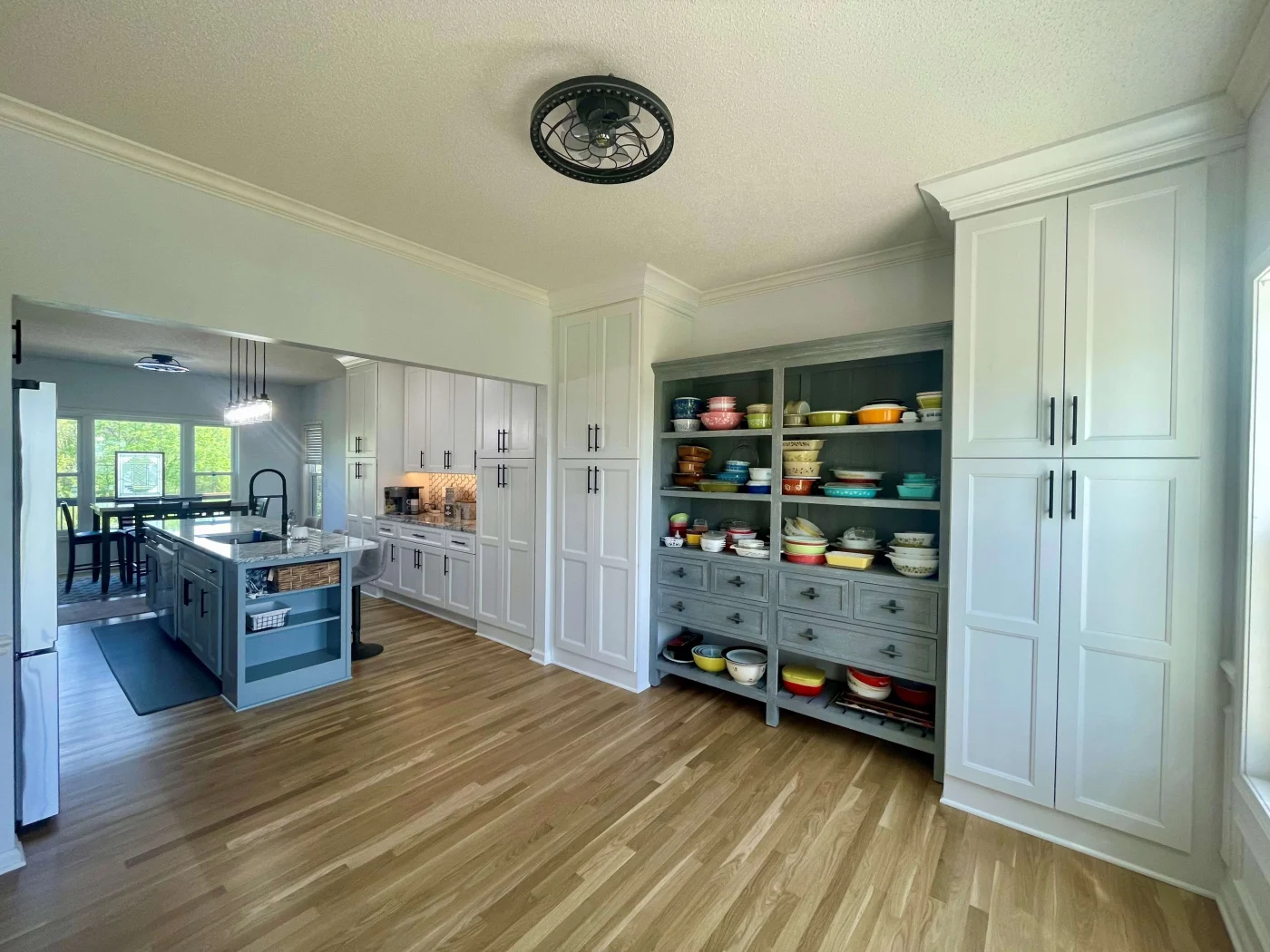 A kitchen with large white cabinets, gray shelves with cabinets, and a kitchen island with a marble countertop.