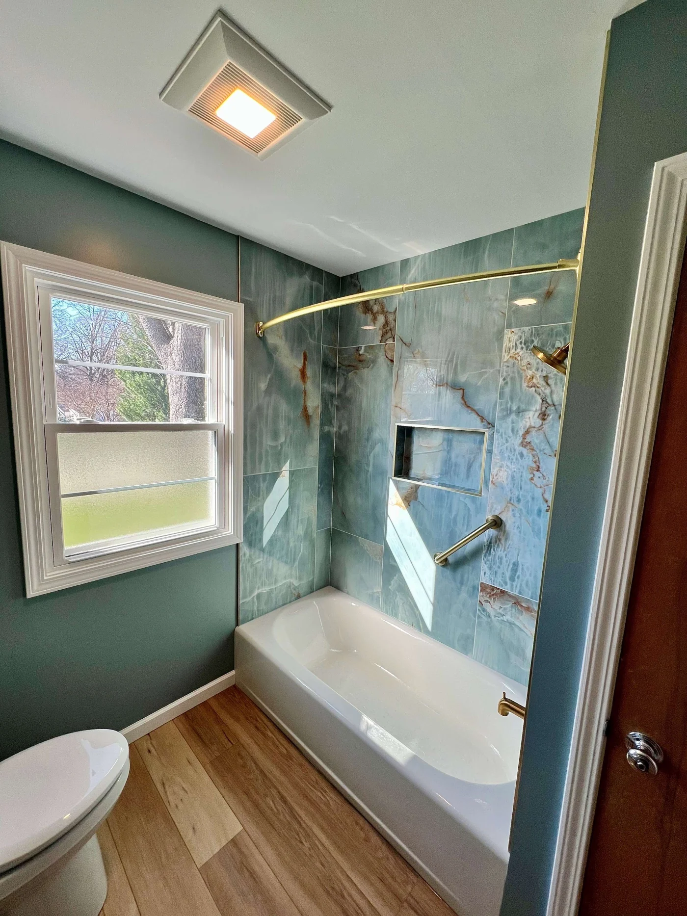 A white bathtub in a teal bathroom with gold fixtures and a grab bar on the far wall.