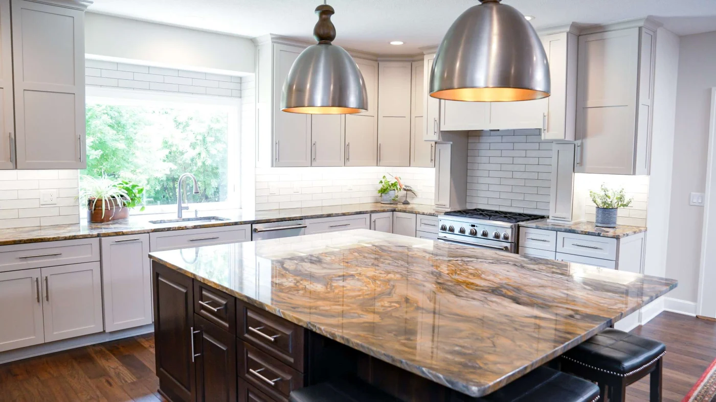 A spacious kitchen with white cabinets, and an island with brown cabinets and overhead lighting.