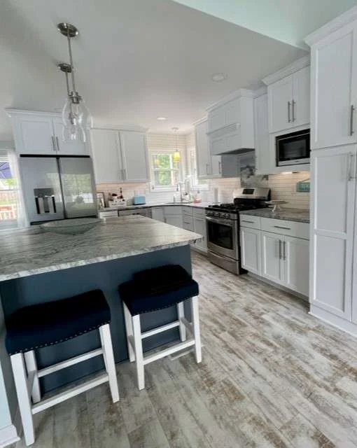 This beautifully bright space features a dark blue island with barstools, striking granite countertops, and clean white cabinetry, highlighting a successful kitchen remodeling project.