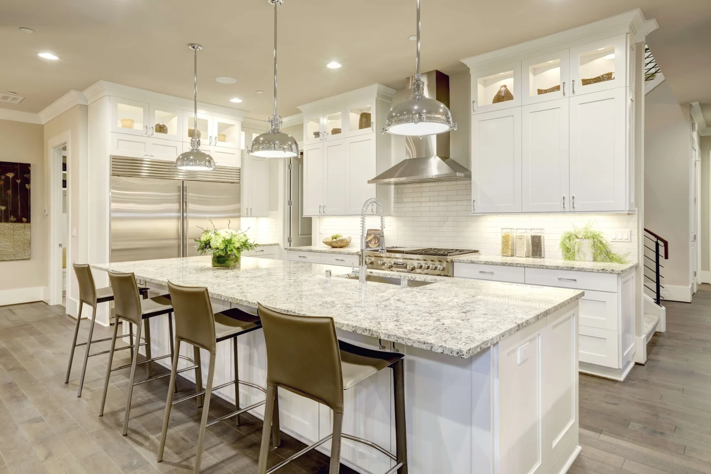 This contemporary kitchen remodel boasts sleek white cabinetry, stainless steel appliances, and a massive granite-topped center island illuminated by industrial pendant lights and lined with modern barstools.