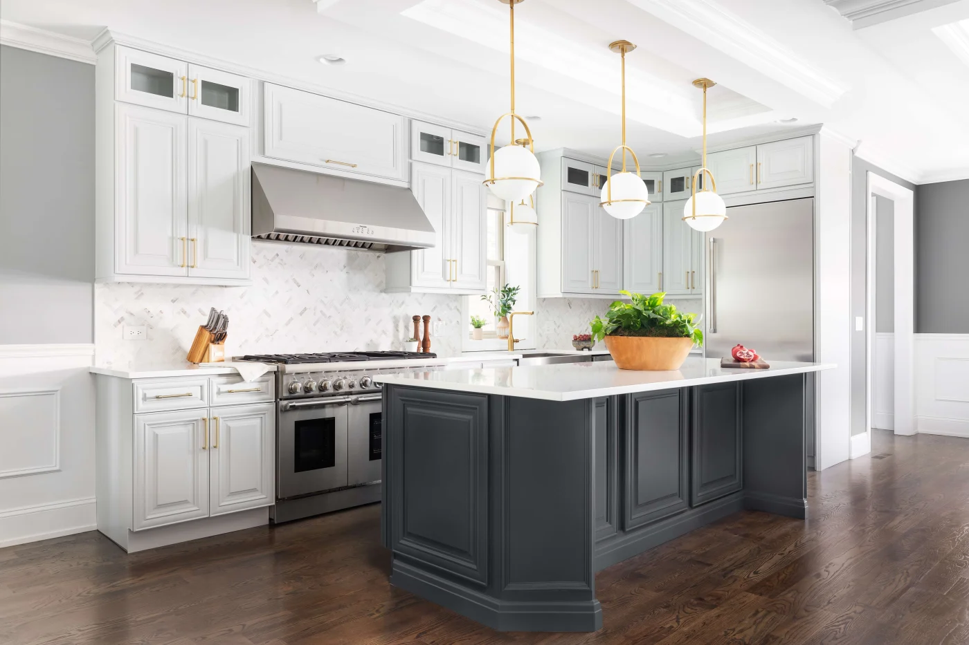 This luxurious kitchen pairs bright white perimeter cabinetry and a striking dark gray center island with elegant gold light fixtures and a marble herringbone backsplash, showcasing the masterful craftsmanship of a top-ranked home improvement contractor.